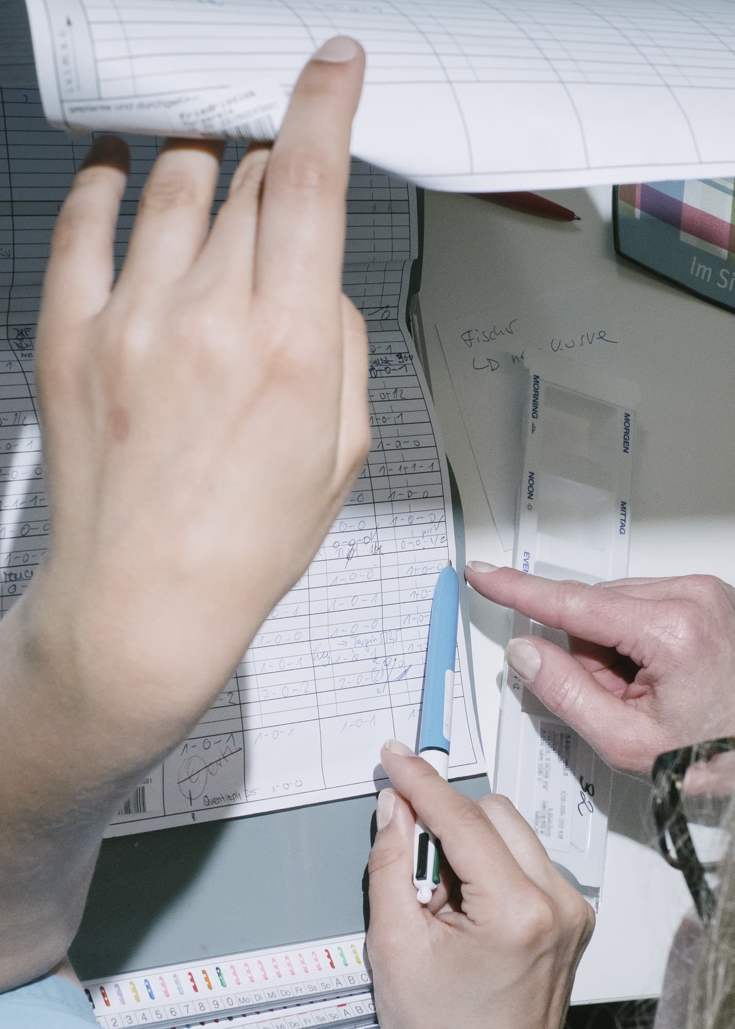 Nicht muede werden — hand detail of two nurses checking documentation on a table